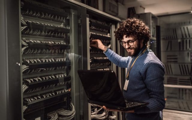 Business Man adjusting server rack while holding laptop