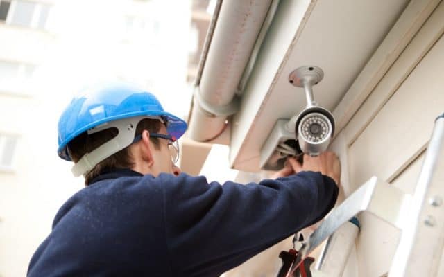 Man wearing hardhat installing ToledoTel security camera.